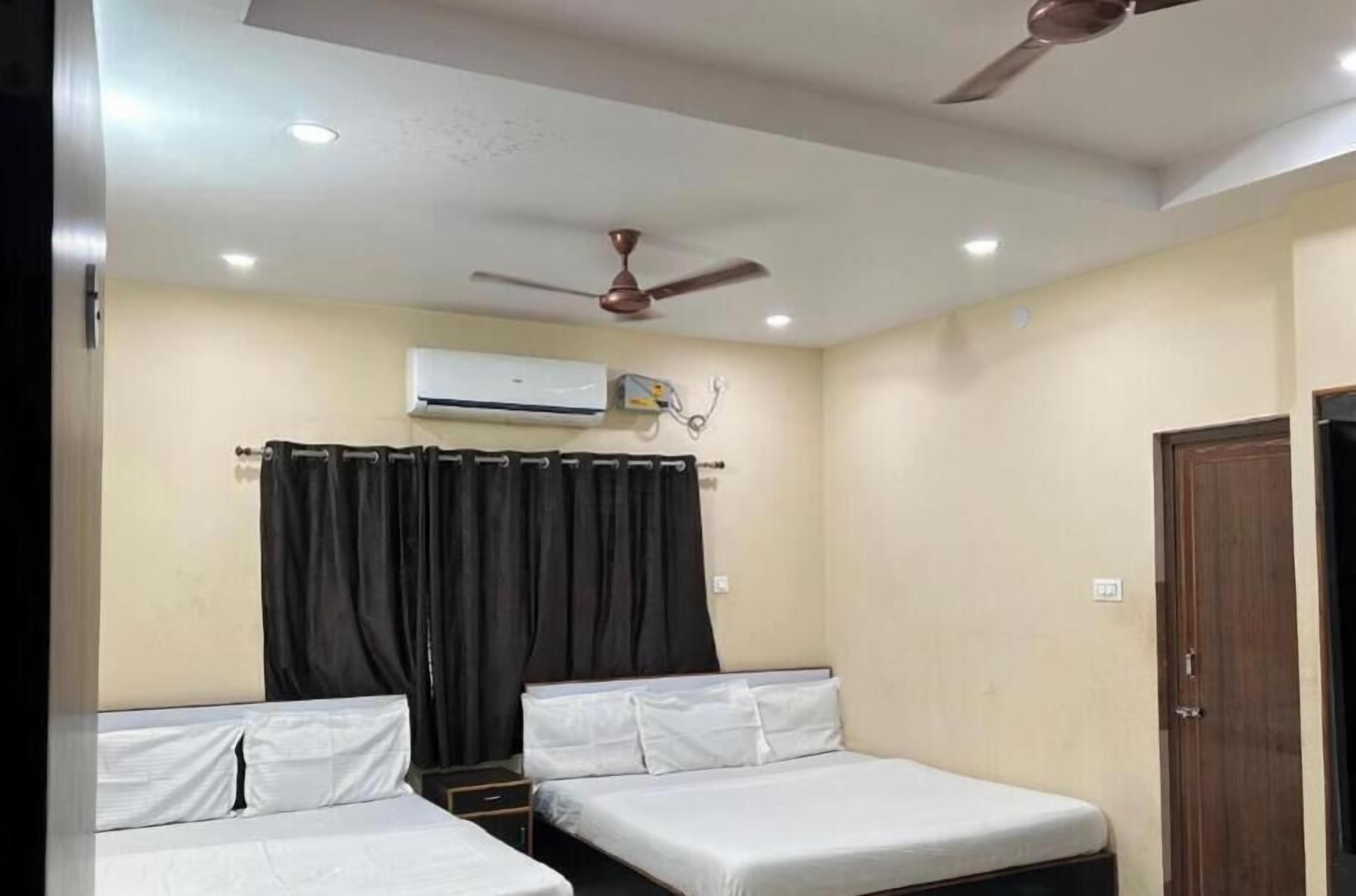 A room with two single beds, a ceiling fan, an air conditioning unit, and a door.
