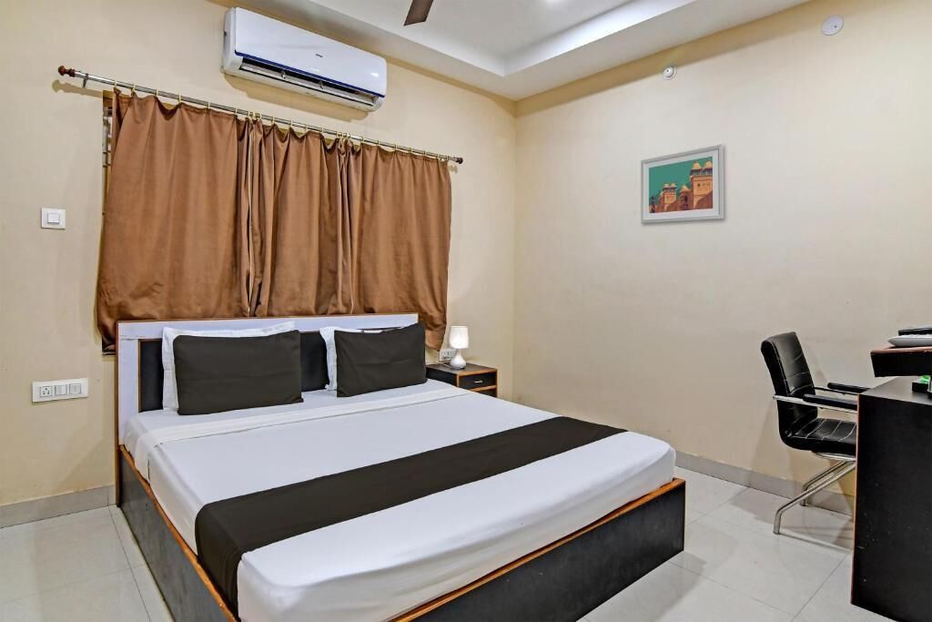 A hotel room with a bed, a desk, a chair, an air conditioner, and a picture on the wall.
