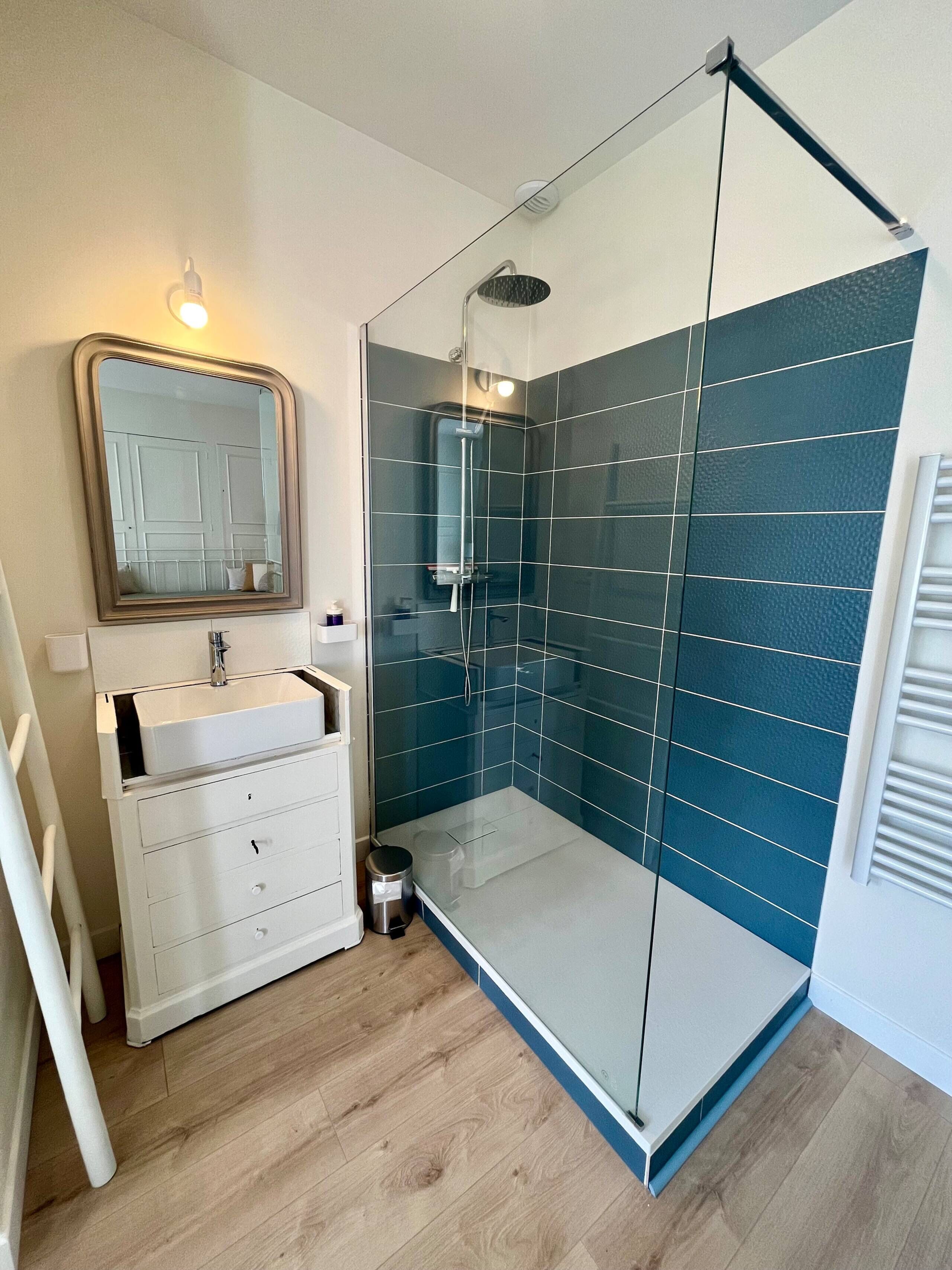 A modern bathroom with a glass shower enclosure, a white vanity with a mirror, and a wooden floor.