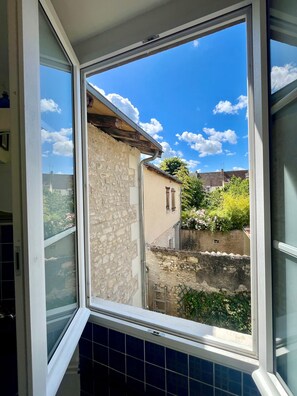 Ein Fenster mit Blick auf ein Steinhaus und einen strahlend blauen Himmel.
