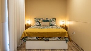 Un lit simple avec une couvre-lit jaune et des oreillers à motifs de feuilles, deux lampes de chevet et une table de chevet blanche.
