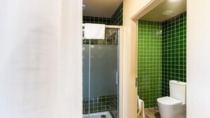 Une salle de bain avec une douche à parois de verre, des toilettes blanches et des murs recouverts de carreaux verts.
