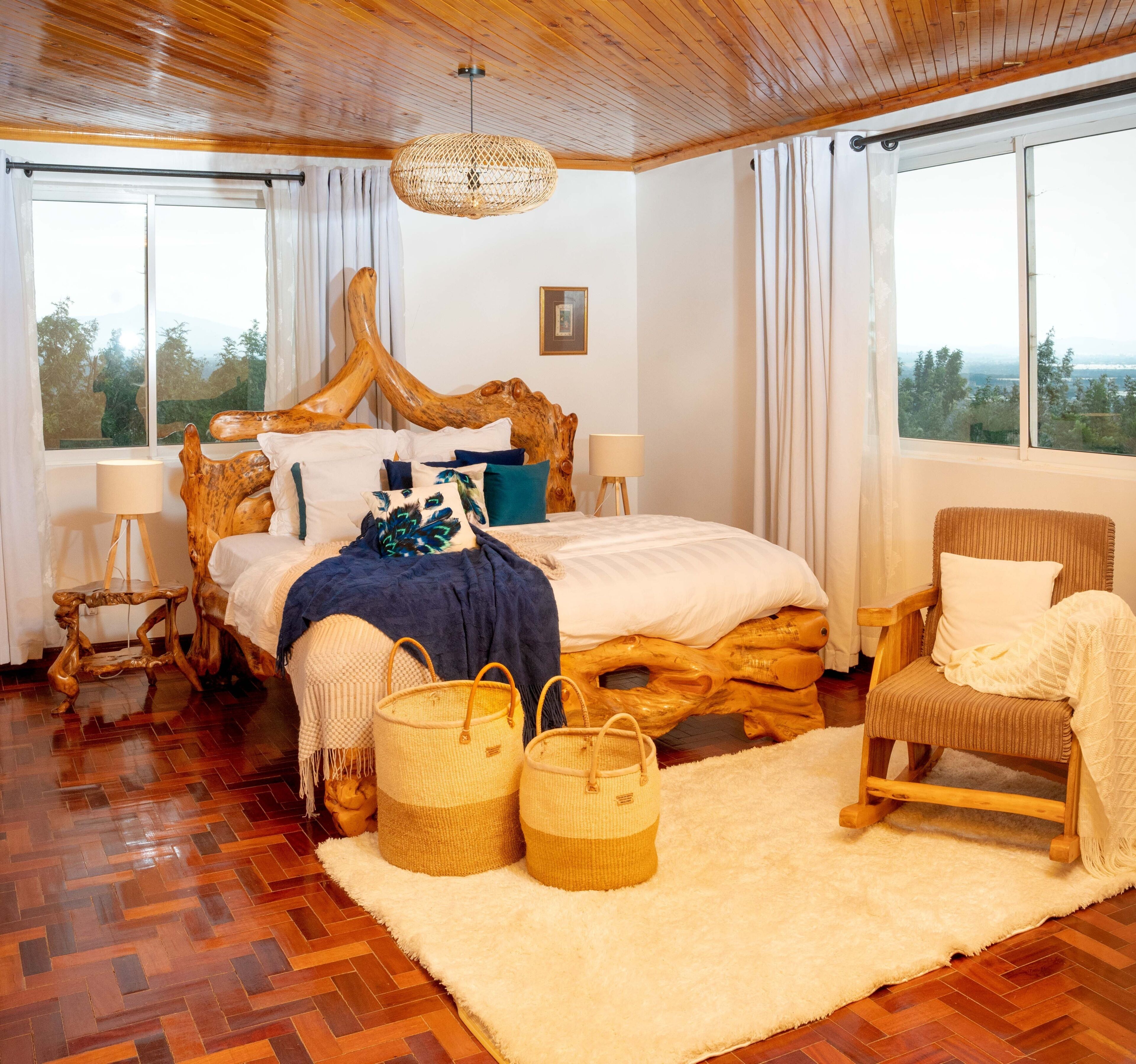 A bedroom with a wooden headboard, a large bed, a chair, a standing lamp, and a view through the window.