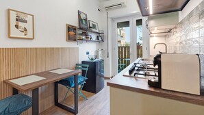 Une cuisine compacte équipée d’une cuisinière à gaz, d’un four encastré et d’un four à micro-ondes. On y trouve un coin repas avec une table et des chaises, ainsi qu’un petit coin salon avec un fauteuil.