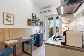 Eine kompakte Küche mit Gaskochfeld, Backofen und Mikrowelle. Ein Essbereich mit Tisch und Stühlen sowie eine kleine Sitzecke mit einem Sessel.