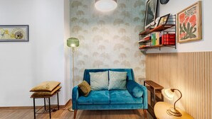 Une pièce avec un canapé bleu, un lampadaire, une bibliothèque et un tableau encadré accroché au mur.