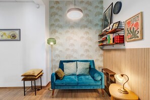 Ein Zimmer mit einem blauen Sofa, einer Stehlampe, einem Bücherregal und einem gerahmten Bild an der Wand.