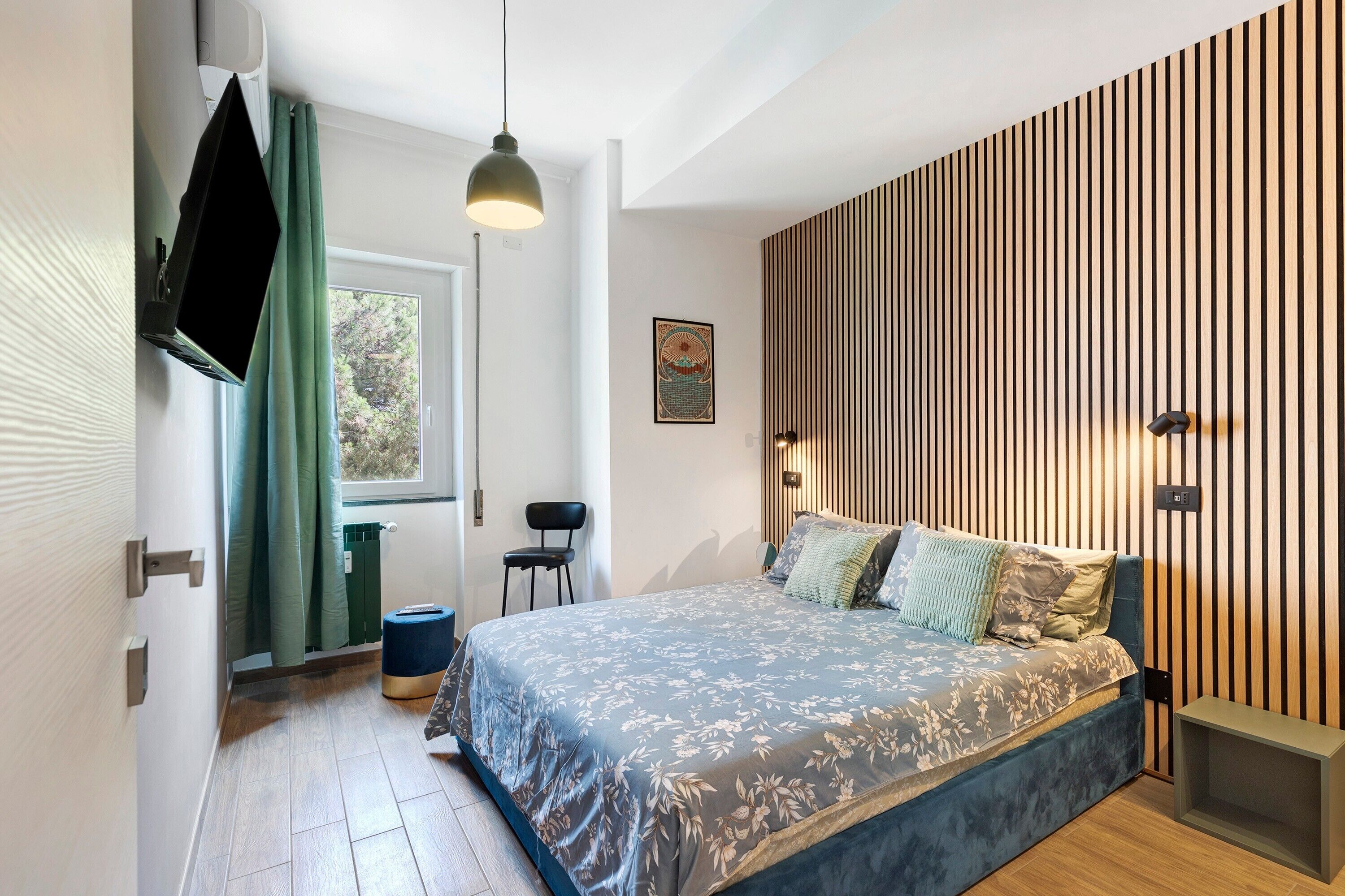Une chambre moderne avec un grand lit, un téléviseur fixé au mur, une fenêtre avec des rideaux et un mur avec des lambris en bois.