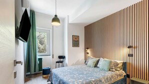 Une chambre moderne avec un grand lit, un téléviseur fixé au mur, une fenêtre avec des rideaux et un mur avec des lambris en bois.