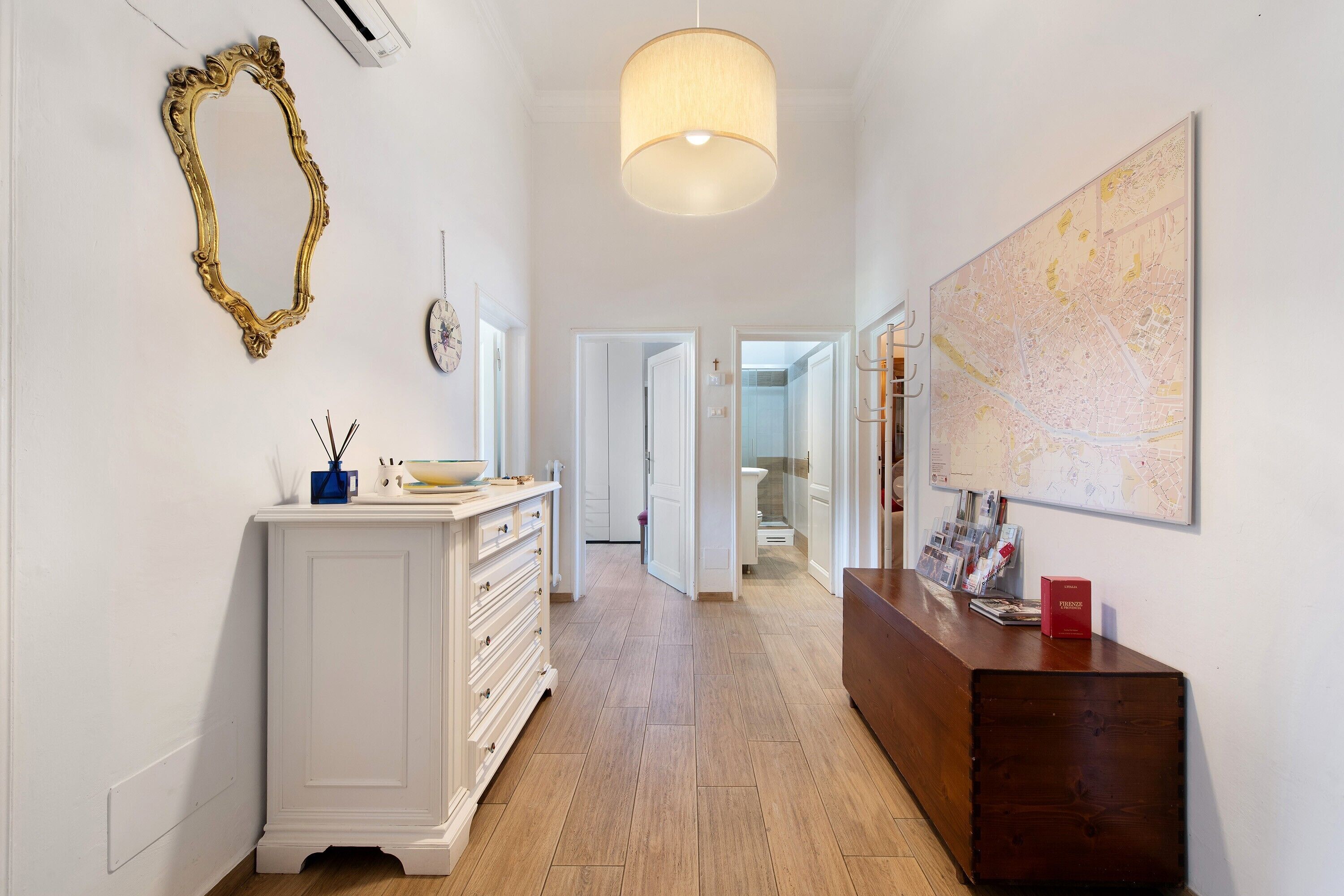 A hallway with a white cabinet, a wooden bench, a map on the wall, and a door leading to another room.