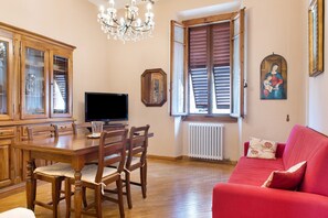 Ein Essbereich mit Holztisch und -stühlen, einem Fernseher und einer Kristallleuchtre.