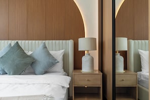 A neatly made bed with pillows, a bedside table with a lamp, and a mirror reflecting the room. - Gala Guests - Binghatti Onyx Suites (Jumeirah Village Circle)