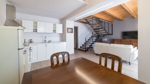 Eine moderne Küche mit weißen Schränken, einem Esstisch mit Stühlen, einer Treppe zu einem Wohnbereich mit einem weißen Sofa und einem Fernseher.