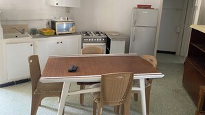 Una cocina compacta con electrodomésticos básicos, una mesa de comedor con sillas y un refrigerador pequeño.