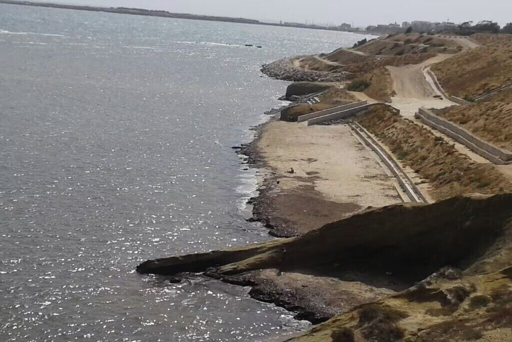 Ett kustområde med en sandstrand, en grusväg och en stenig strandlinje.