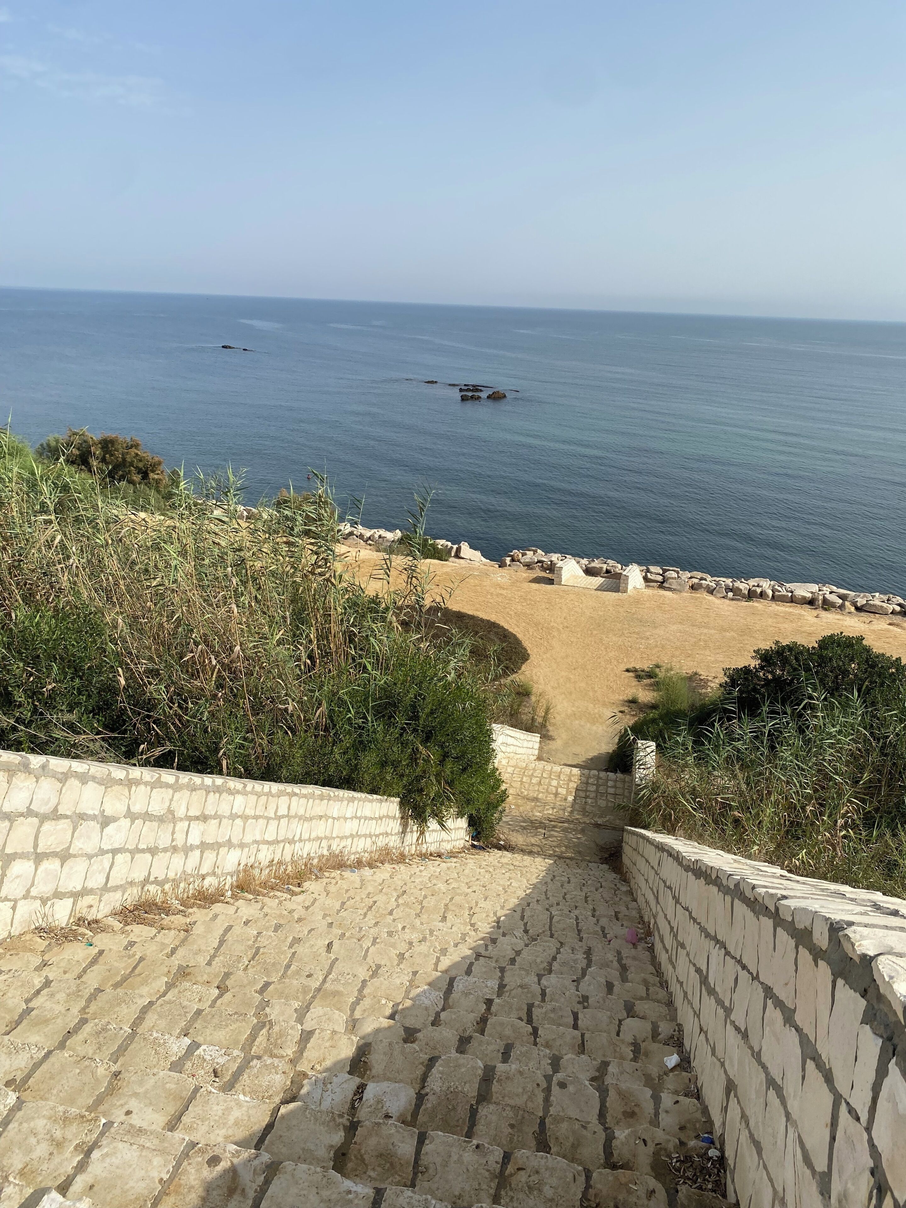 A stone staircase leading to a beach with a clear view of the sea.