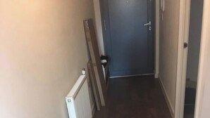 Un pasillo estrecho con suelo de madera, un radiador y una puerta al final.