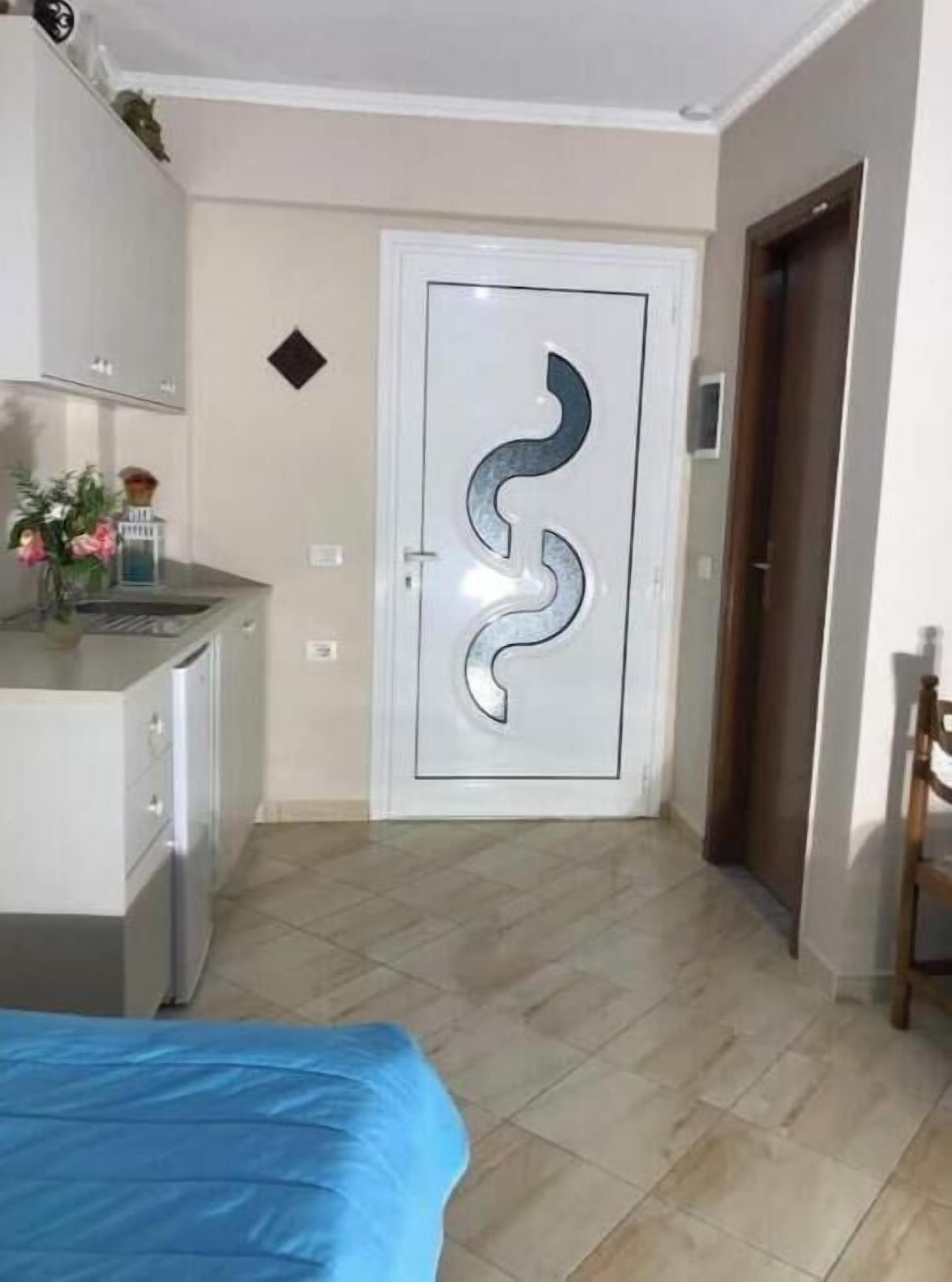 A room with a bed, a kitchenette, and a door with a unique design.