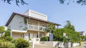 Un edificio residencial de dos plantas con balcón, garaje y un jardín bien cuidado.