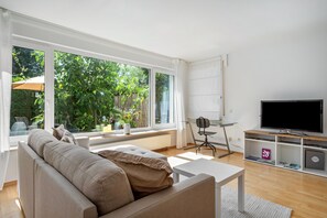 Ett modernt vardagsrum med en soffa, ett soffbord, en tv och ett stort fönster med utsikt över grönområden.
