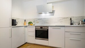 Una cocina moderna con armarios blancos, horno integrado y cafetera.