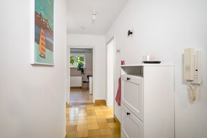 A hallway with a tiled floor, a white cabinet with a telephone, and a door leading to a room with a window. - 'Das.møyn' – Your Stay with Mr. Max & Miss Tilda (Friedrichshafen)