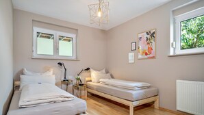Un dormitorio con dos camas individuales, una mesita de noche con lámpara, una ventana con vistas a zonas verdes y un cuadro colgado en la pared.