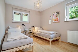 Ein Schlafzimmer mit zwei Einzelbetten, einem Nachttisch mit Lampe, einem Fenster mit Blick auf Grünflächen und einem Wandbild.