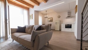 A modern living room with a sofa, a dining table, and a kitchen in the background. - Casale dei Sogni Entire Private Villa with Terrace, Wi-Fi, and Air Conditioning (Cavaion Veronese)