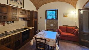 A kitchen with wooden cabinets, a dining table with a tablecloth, a red sofa, and a stone wall. - Casina di Gabry (Toscana)