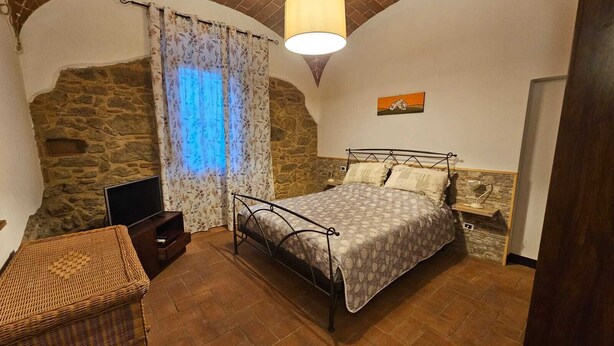 A bedroom with a stone wall, a bed, a lamp, and a television. - Casina di Gabry (Toscana)