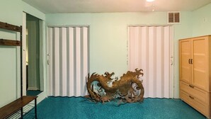 Una habitación con ventilador de techo, dos puertas con persianas verticales, un banco de madera y una escultura metálica decorativa de gran tamaño.