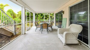 Un patio techado con una mesa y sillas, un sofá de mimbre y vistas a la vegetación.