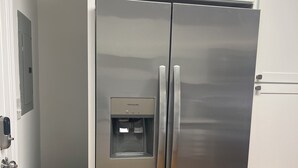 Un refrigerador de acero inoxidable con dispensador de agua, un cubo de basura y un armario blanco.