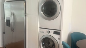 Una cocina compacta con un refrigerador de acero inoxidable, una lavadora y una silla color turquesa.