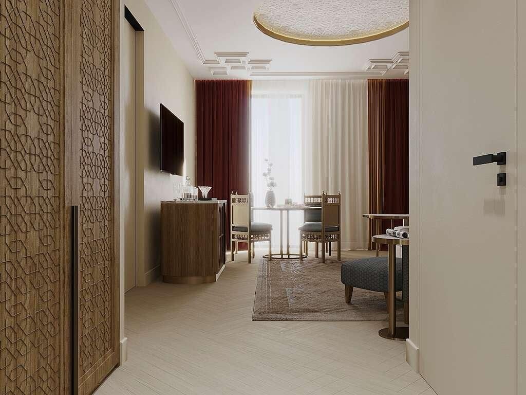A hotel room with a wooden partition, a flat-screen TV, a desk with a chair, a small table, and a sofa.