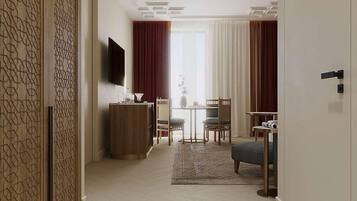 A hotel room with a wooden partition, a flat-screen TV, a desk with a chair, a small table, and a sofa.