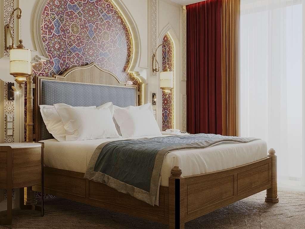 A bed with a wooden frame and white bedding, a nightstand with a lamp, and a decorative wall with intricate patterns.