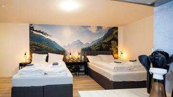 A hotel room with two beds, a wooden floor, a large mountain view mural, and a small table with a coffee pot.