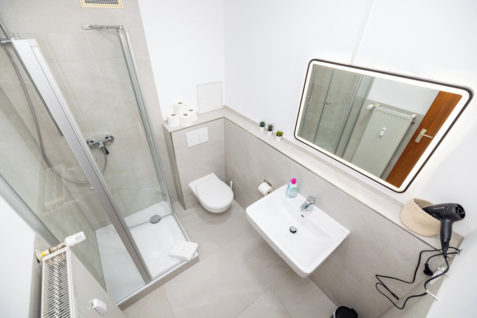 A modern bathroom with a glass shower enclosure, a white toilet, a sink with a mirror above, and a hairdryer on the wall.