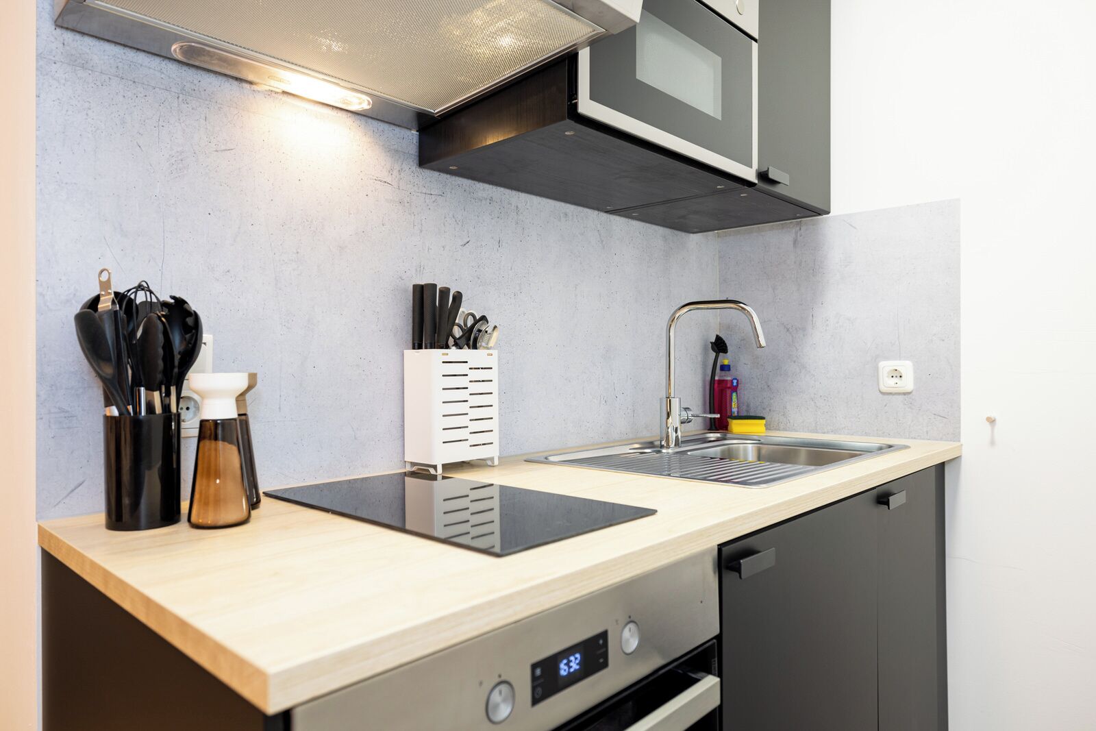 Cocina compacta con microondas, horno y lavavajillas, un lavabo con grifo y una encimera con utensilios y especias.