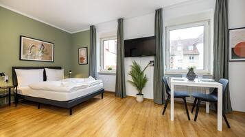A room with a bed, a desk, a chair, a potted plant, and a TV.