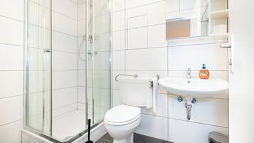 A modern bathroom with a glass shower enclosure, a white toilet, and a sink with a soap dispenser.