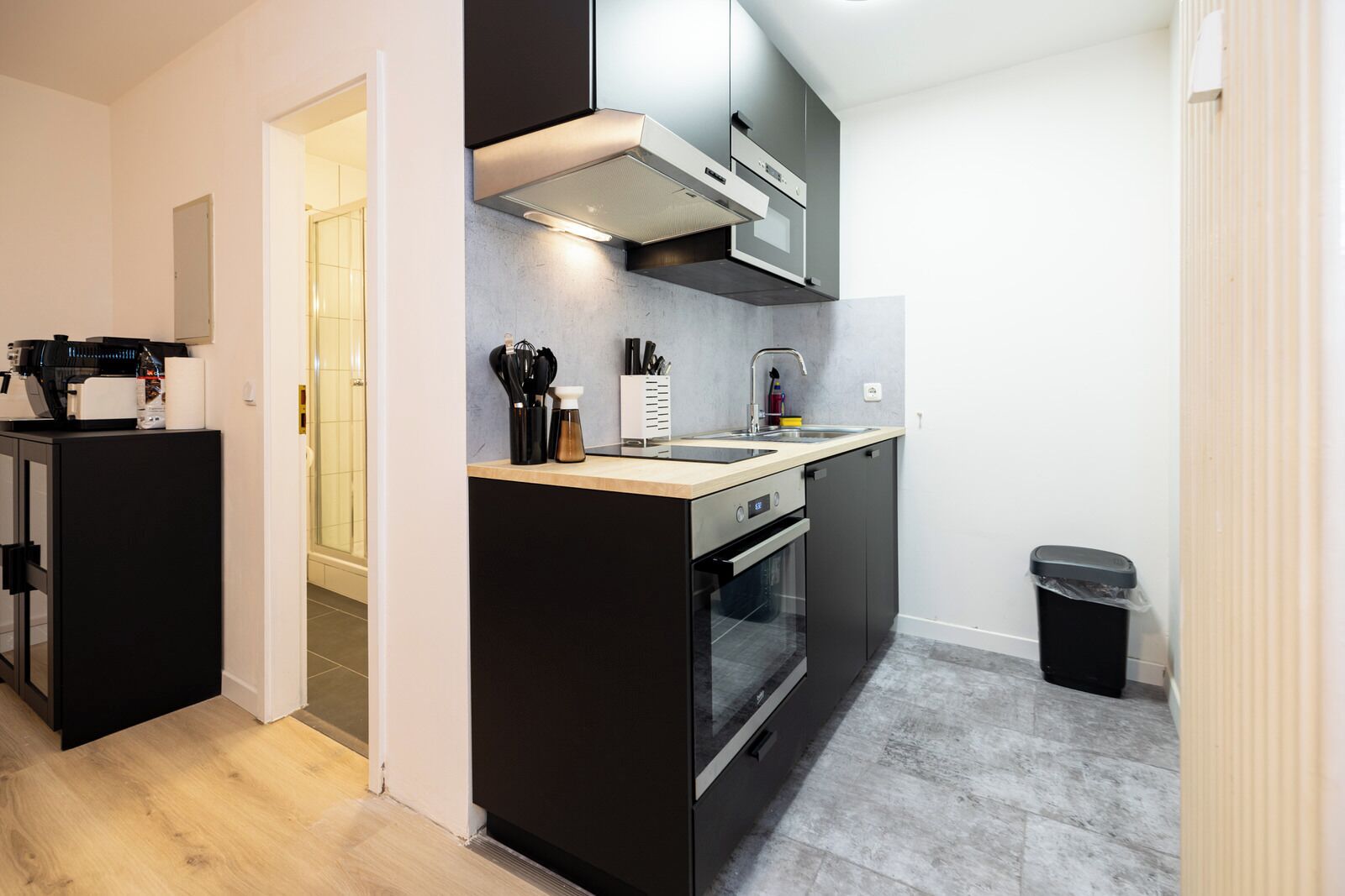 A compact kitchen with a built-in oven, a sink, and a trash bin.