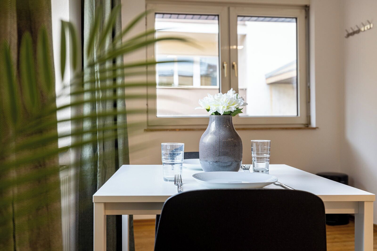 A dining table with a vase of flowers, two glasses, and a plate.