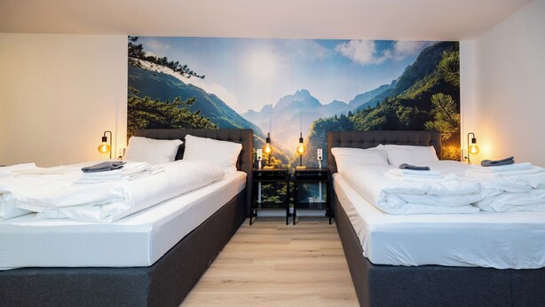 Habitación de hotel con dos camas, piso de madera y un mural con vistas a la montaña.
