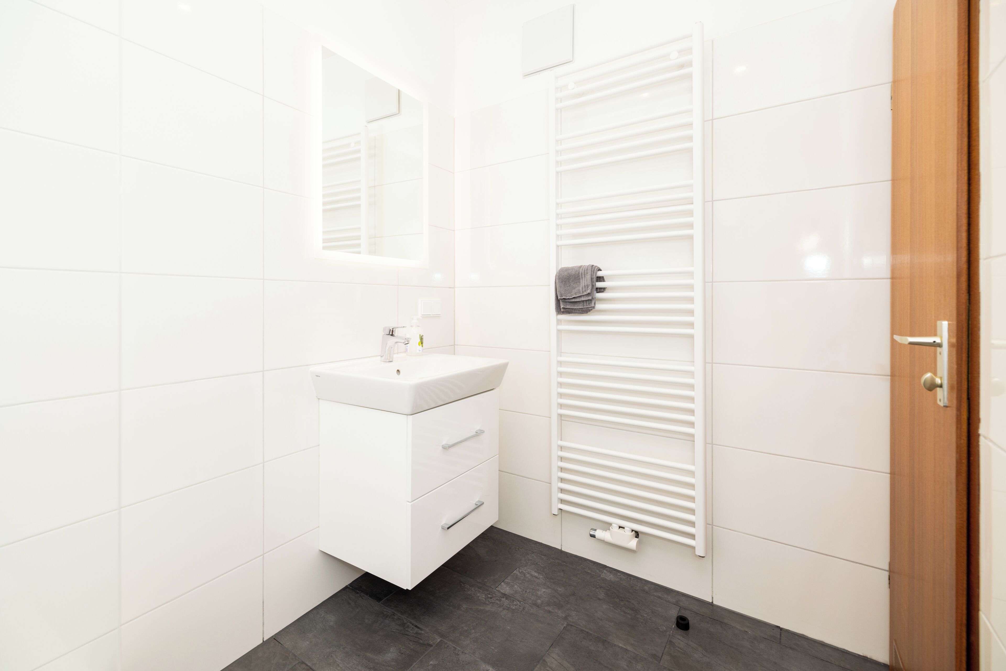Une salle de bain moderne avec des carreaux blancs, un lavabo blanc, un miroir et un porte-serviettes.