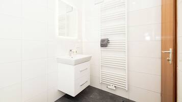 Une salle de bain moderne avec des carreaux blancs, un lavabo blanc, un miroir et un porte-serviettes.