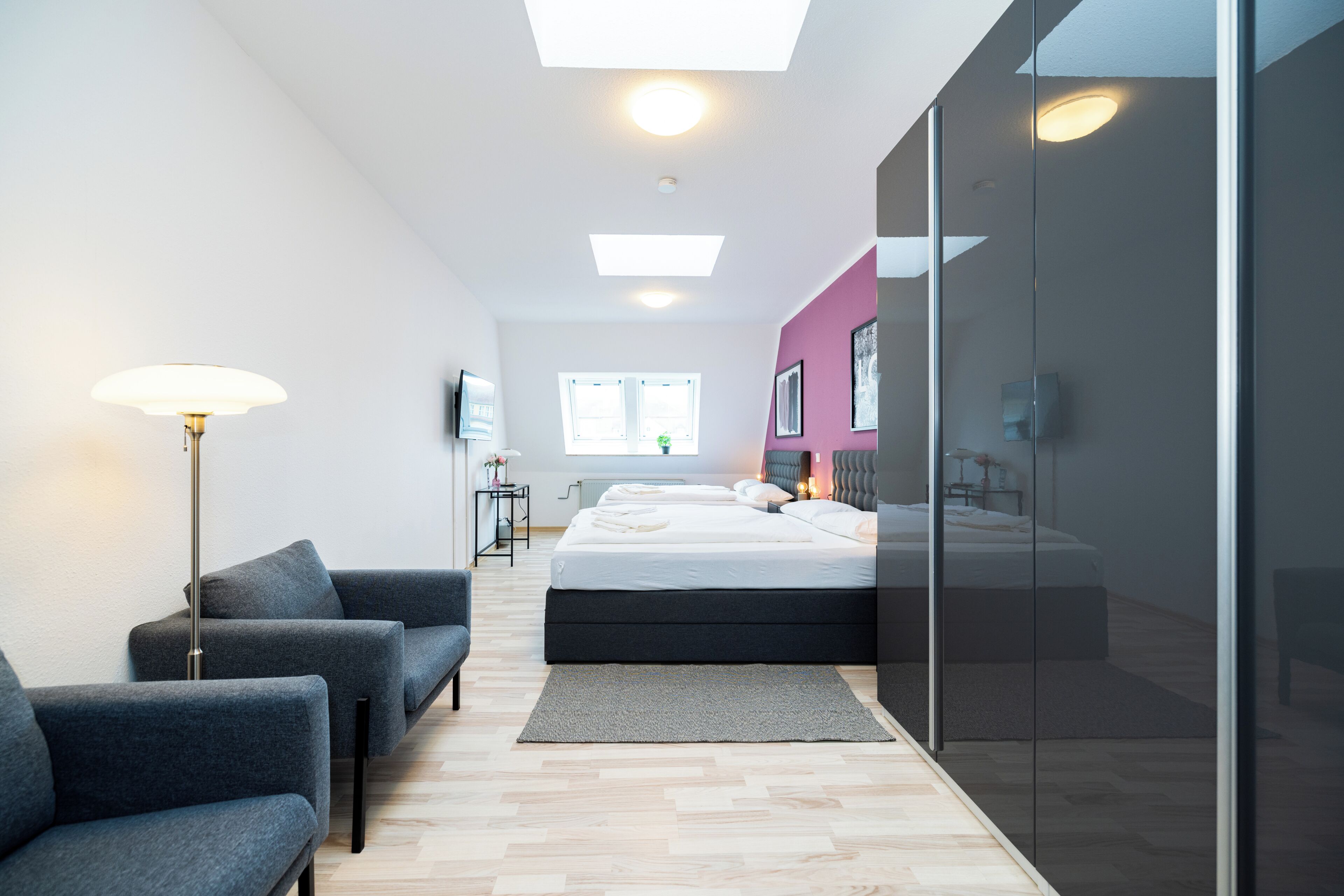 A modern bedroom with a bed, a sofa, a floor lamp, and a large window.