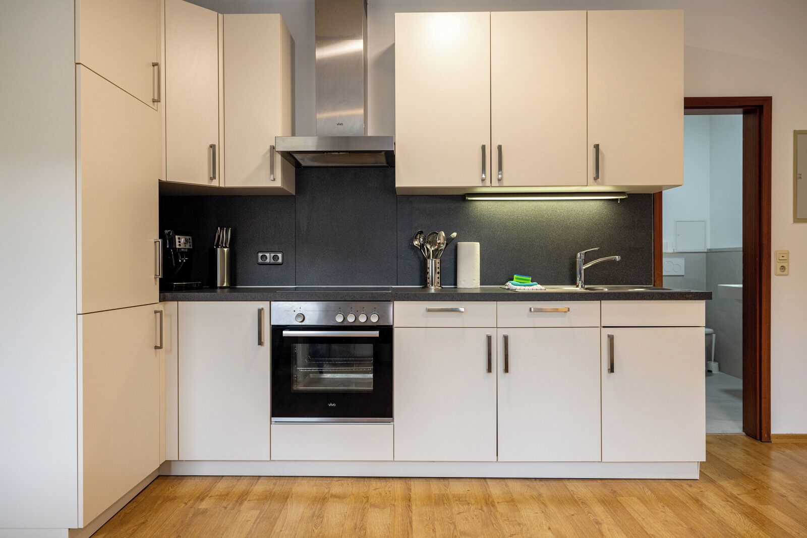 A modern kitchen with white cabinets, a black oven, a stainless steel range hood, and a black countertop.